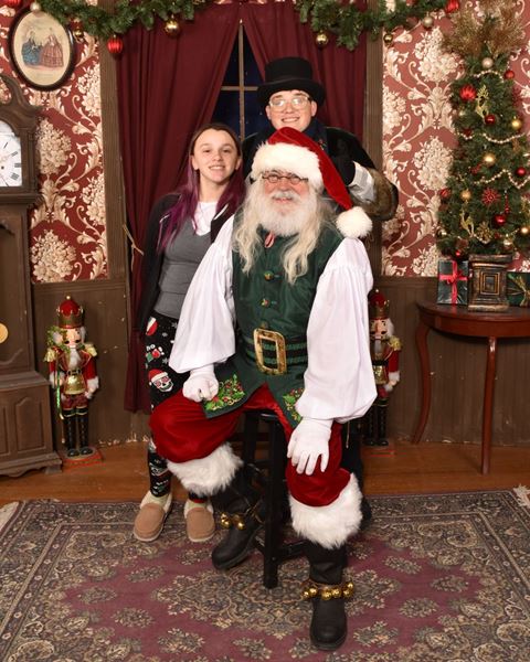 Two teens behind a seated Santa, one in a Victorian top hat